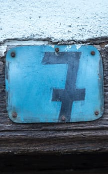 Rustic house number 7. Hand-painted blue sheet metal nailed to the wooden lintel of the door