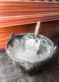 Bucket full white adhesive mortar ready for applicate. Large thin-walled hollow bricks as background
