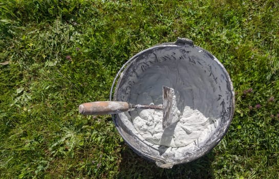 Bucket full white adhesive mortar ready for applicate. Green grass as background