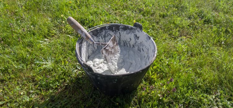 Bucket full white adhesive mortar ready for applicate. Green grass as background