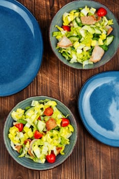 Delicious salad with green, cucumber, tomatoes and pieces of roasted meat on wooden table.