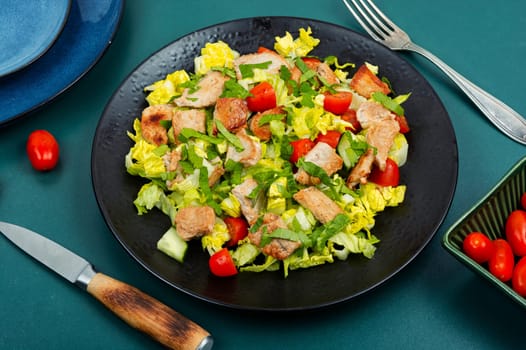 Salad with green lettuce, cucumber, tomatoes and pieces of meat. Top view.