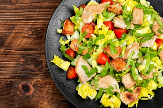 Salad with green lettuce, cucumber, tomatoes and pieces of meat. Top view.
