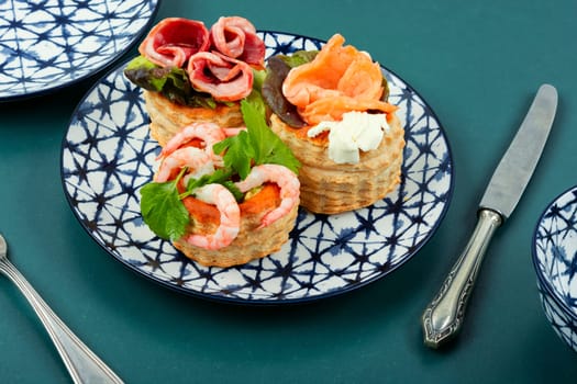 Puff pastry tartlets or canapes with fish, shrimp and bacon on a plate on the table.