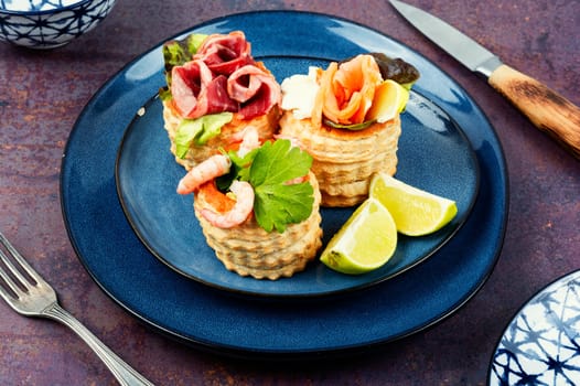 Puff pastry tartlets or canapes with fish, shrimp and bacon on a plate on the table.