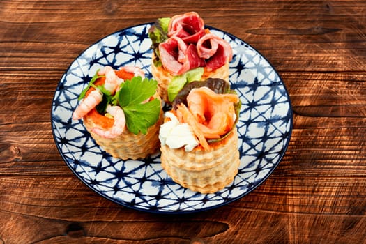 Puff pastry tartlets or canapes with fish, shrimp and bacon on a plate on the table.