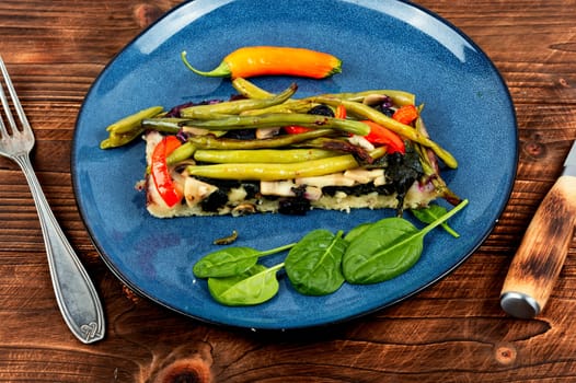 Piece vegetable homemade pie with green or bush beans and peppers on rustic wooden background.