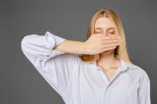 Young woman with closed eyes covers her mouth with her palm