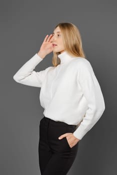 Young woman stands in profile with her hand to her ear, listening