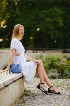 Young blonde woman sits in profile on a bench