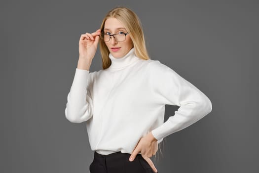 Young serious woman holding glasses by the temple while looking at the camera