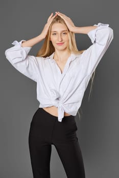Young blonde woman in a shirt tied at the waist posing with her hands raised to her head