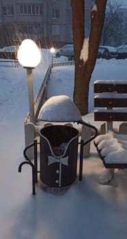 A figurative trash can in the form of a tailcoat and a hat in the snow in winter. Decorating a trash can near the entrance. Winter in the city. Snow cover on the trash can
