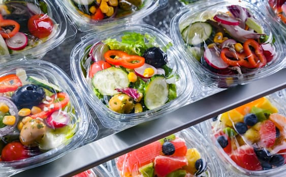Plastic boxes with pre-packaged vegetable salads, put up for sale in a commercial refrigerator