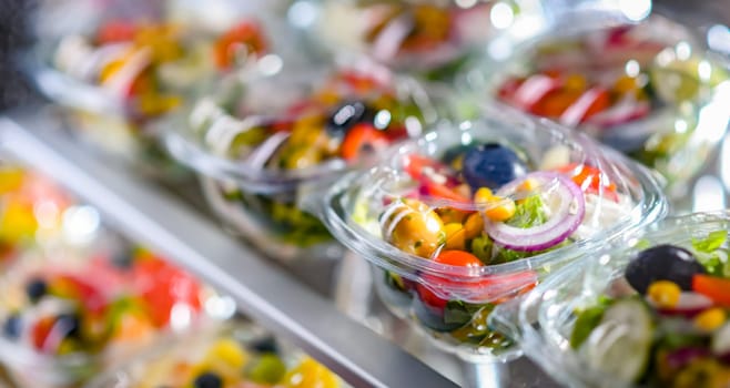 Plastic boxes with pre-packaged vegetable salads, put up for sale in a commercial refrigerator