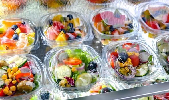Plastic boxes with pre-packaged fruit and vegetable salads, put up for sale in a commercial refrigerator
