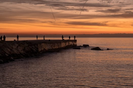 Mediterranean landscape at sunrise. People fishing, walking or exercising at the Espigó del Gas (Gas Breackwater), on the waterfront in Barcelona, Spain.