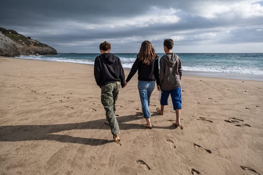 A parent and two young sons walking together along a deserted beach, rear view. Conceptual theme of doing fun things together and taking time to relax, reconnect within the family.