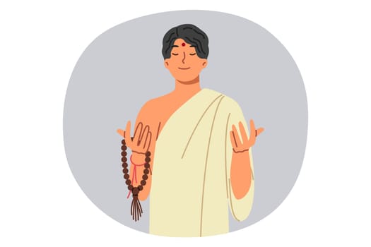 Asian muslim man in traditional ethnic clothing prays and meditates, holding rosary in hands. Muslim guy from countries of pan-asian region with dot on forehead, smiles and closes eyes