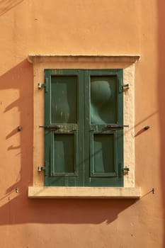 Window of a colorful house with green closed shutters in the old town of Malcesine on Lake Garda in Italy