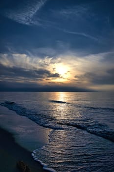 Sunset, illuminated sea. Sandy beach in the foreground. Light waves. Baltic Sea. Landscape on the coast