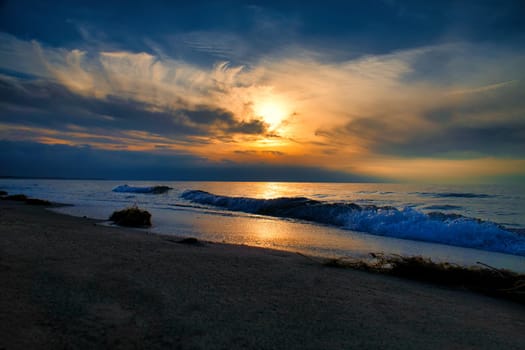 Sunset, illuminated sea. Sandy beach in the foreground. Light waves. Baltic Sea. Landscape on the coast