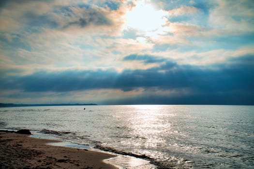 Sunset, illuminated sea. Sandy beach in the foreground. Light waves. Baltic Sea. Landscape on the coast