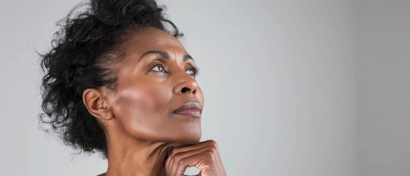 A mature woman with natural grey hair looks away thoughtfully, her hand on her chin. Her expression is one of reflection and poise