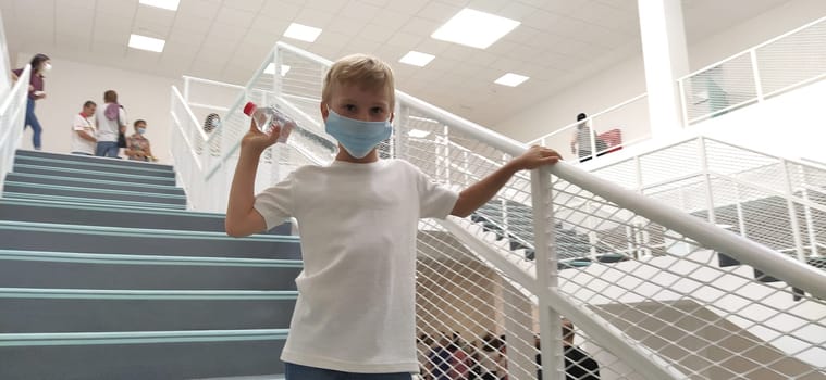 Sremska Mitrovica, Serbia, September 1, 2020. A boy in a white shirt and a mask poses on the stairs. A child of 7 years old holds onto the handrail. Modern school, clinic or hospital with white walls.