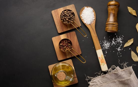 Salt, allspice, peppercorns and olive oil in a bottle on a black table, top view