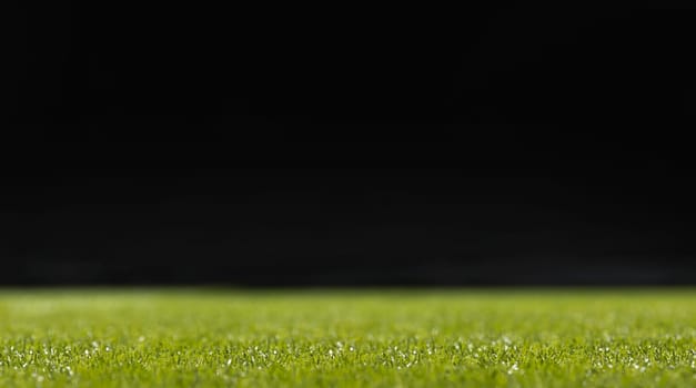 A selective background of green grass at the bottom of the frame with dew drops on a black background