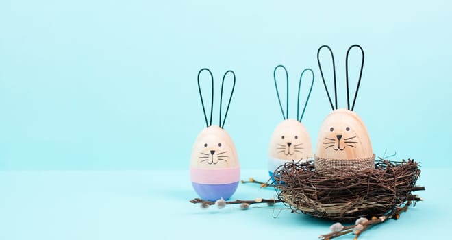 Easter bunny or rabbit sitting in a bird nest, willow branches, wooden egg, spring holiday, blue color