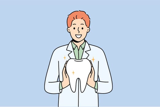 Man orthodontist from dental clinic holds model of healthy tooth, offering you procedure to get rid of caries. Guy orthodontist in white coat smiles, recommending becoming client of new dental center