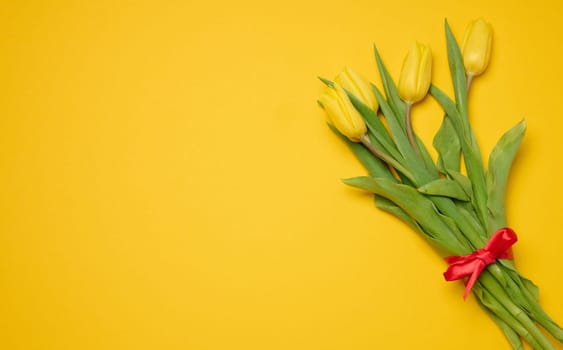 Bouquet of blooming tulips with green leaves on a yellow background, top view. Copy space