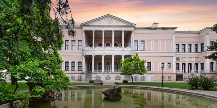 Twilight bathes the National Painting Museum with a warm glow, reflecting in the courtyards tranquil pond at Dolmabahce Palace, Istanbul, Turkey