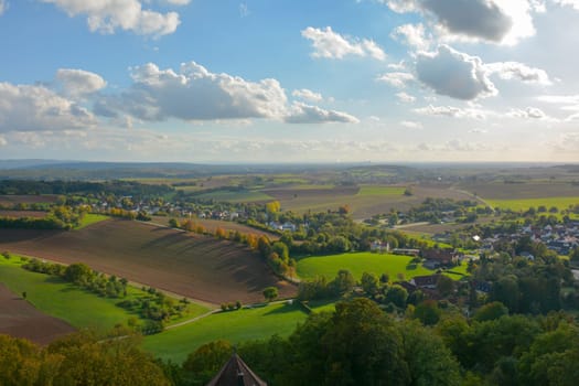 Top view of a green landscape with houses of a village, farmland, forest and blue sky