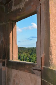 View through an old castle window on a blue sky with white clouds and green landscape