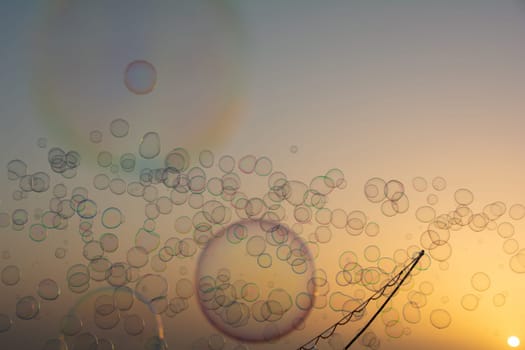 Lots of colorful soap bubbles floating in the orange sky at sunset with soap bubble stick