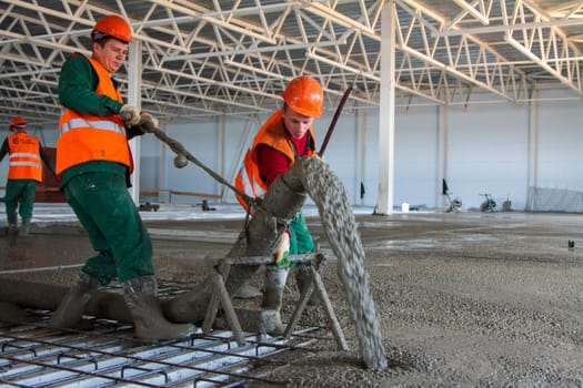two Caucasian workers pouring concrete floor in large industrial hangar building in Tula, Russia - July 22, 2013