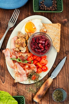 Fried bacon and eggs, toast and beans and vegetables. Traditional English breakfast on a vintage wooden background.