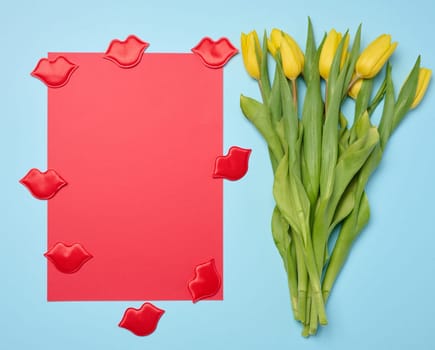 Bouquet of blooming yellow tulips with green leaves on a blue background, top view. Copy space