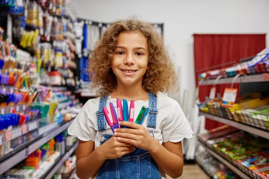 Selective focus school girl holding variety of pens for writing standing at stationery store. Creative tools for education concept