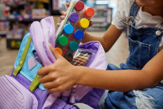 Portrait of lovely smart girl putting paints kit into schoolbag. Shopping before back to school, preparation for education at arts lesson