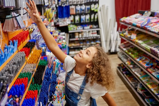 Portrait of little school girl choosing pen at stationery store while preparing for new education year