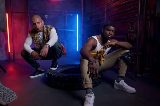 Two young funky multiethnic drug dealers with serious faces posing for camera in neon light