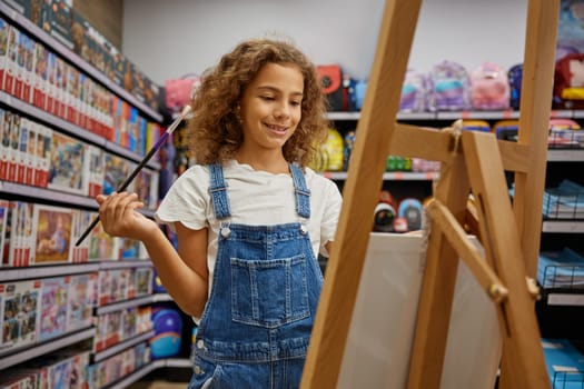 Attractive girl child testing brush painting on canvas easel during shopping for school art class at stationery store