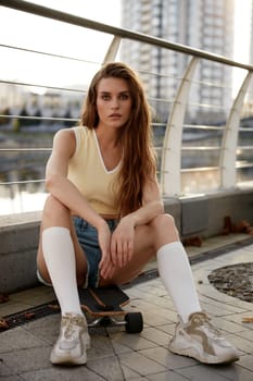 Portrait of young relaxed woman sitting with her longboard after training workout. Sportive leisure activity enjoyment concept
