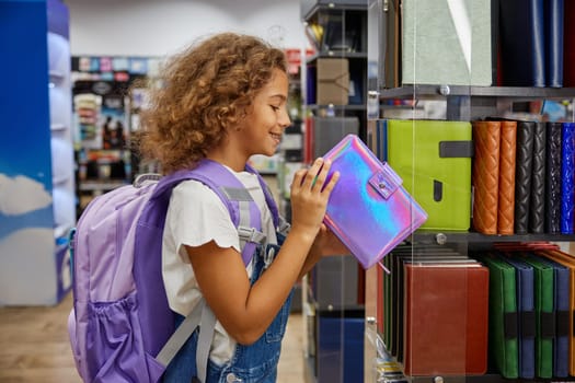 Happy excited girl child searching for school supplies at stationery shop. Female preteen kid choosing colorful bright diary notebook