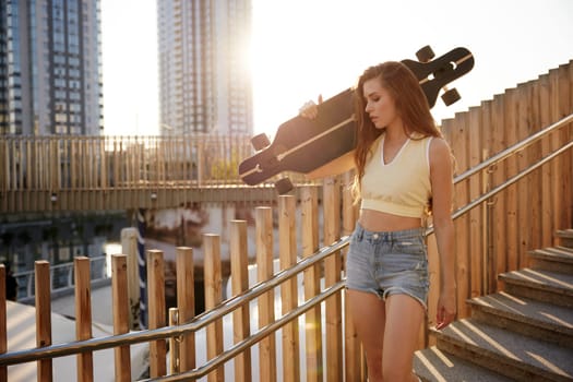 Atmospheric photo of young carefree woman walking down park stairs with longboard. Sports hobby time outdoors enjoyment, trendy fashion and youth urban style