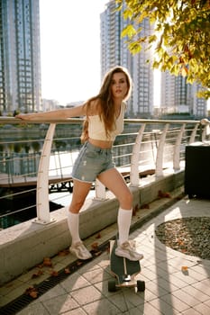Charming young woman wearing casual trendy outfit posing over summer sunset at city park nearby river bank. Happy teenage recreation time